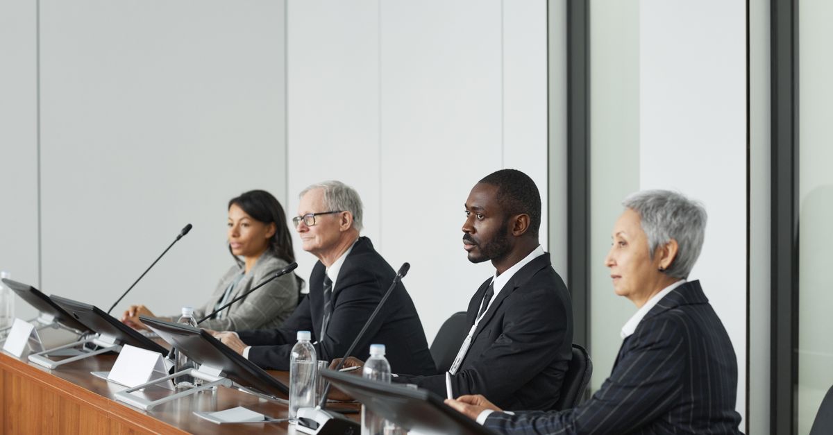 Professional business panel meeting in a modern office setting with four diverse executives seated at a table.